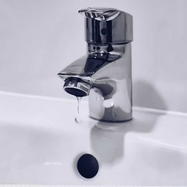 A chrome faucet dripping a single water droplet into a clean white bathroom sink, captured in a close-up shot with a soft, minimalist aesthetic.